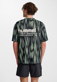 Mörkgrön och svart mönstrad t-shirt med "hummel"-logotyp på baksidan. Tillverkad av lätt material med avslappnad passform och korta ärmar.