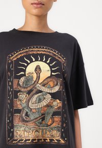 Svart T-skjorte med et fargerikt grafisk design av slanger og blomster, med "RIPCURL"-tekst nederst og intrikate kantdetaljer.