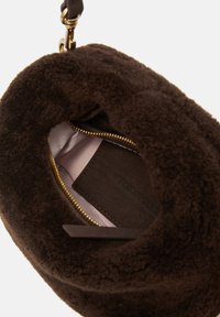 Brown faux shearling bag interior featuring a soft pink lining, gold zipper, and a leather tag with embossed text.