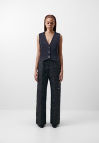 Zkrácená denimová vesta s knoflíkovým zapínáním v tmavě modré barvě, kombinovaná s černými prošívanými kalhotami širokého střihu, které mají decentní logo a stahovací pas.