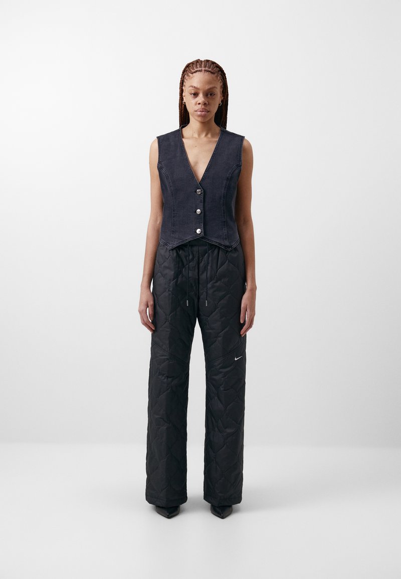 Zkrácená denimová vesta s knoflíkovým zapínáním v tmavě modré barvě, kombinovaná s černými prošívanými kalhotami širokého střihu, které mají decentní logo a stahovací pas.