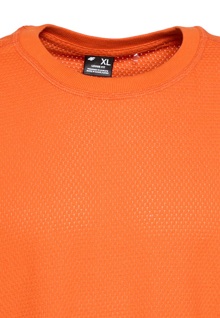 Pomarańczowa, luźno dopasowana koszulka sportowa z heksagonalnym wzorem siateczkowym i metką rozmiaru XL z napisem "Zaprojketowane w Europie, wyprodukowane w Bangladeszu."