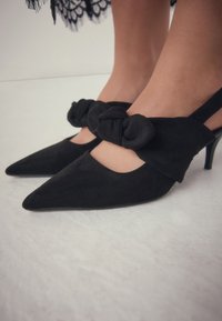 Escarpins à lanières en daim noir avec bouts pointus, ornés d'un noeud noué sur la bride de cheville et talons aiguilles fins.