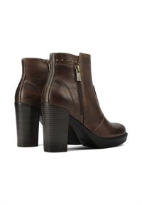 Stivaletti alla caviglia in pelle marrone con punta tonda, chiusura con zip e un robusto tacco texturizzato. Presentano piccoli borchie metalliche lungo il bordo superiore.