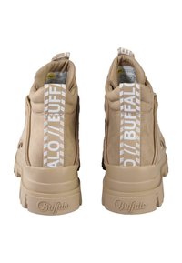 Bottines en daim beige avec une finition texturée, dotées de tirettes logo blanches, de semelles épaisses et de détails de couture contrastés.