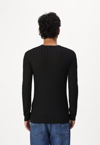 Maglione nero a coste con maniche lunghe, colletto rotondo e polsini aderenti, texturizzato con strisce verticali. Indossato con jeans blu.