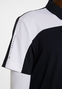 Svart och vit pikétröja med en texturerad krage, skarp färgblockering och logotypdetalj längs ärmen. Slät, lättviktigt material.