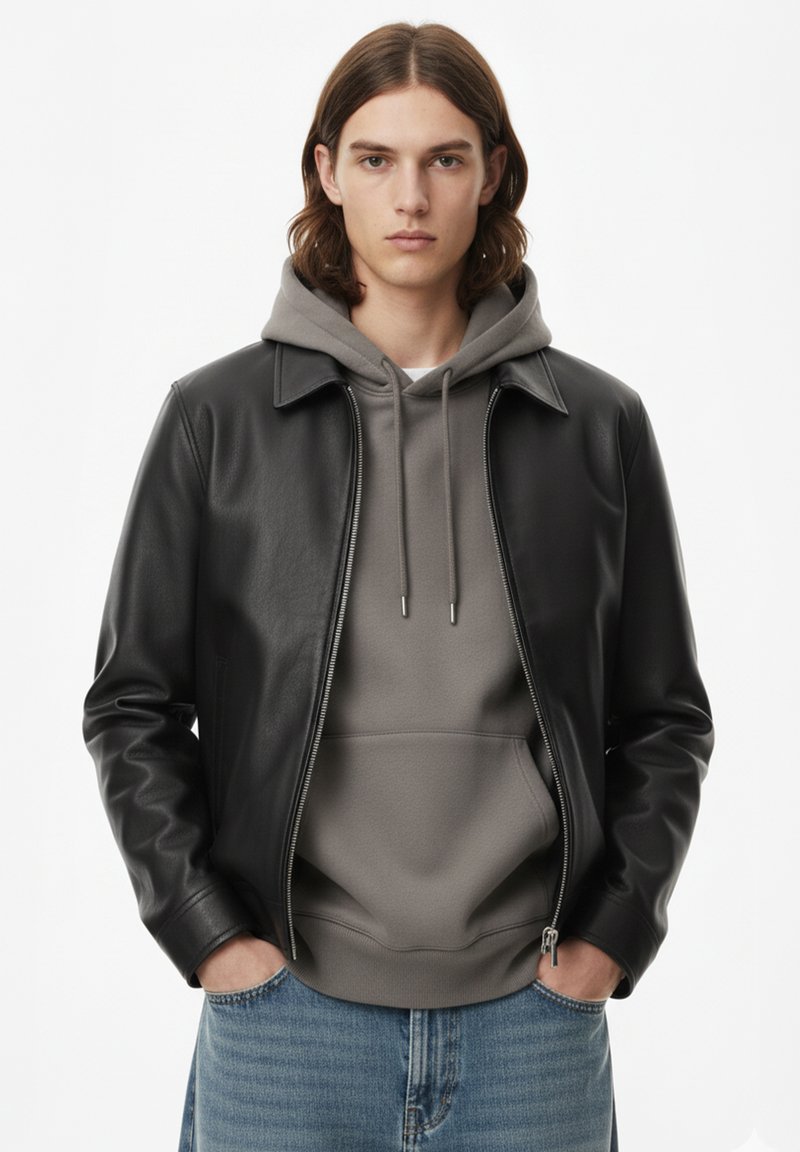 Giacca di pelle nera con collo, indossata sopra una felpa grigia con cappuccio. Modello con capelli lunghi e jeans blu. Dettaglio cerniera sulla giacca.