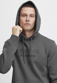 Gray hoodie with a kangaroo pocket, drawstrings, and "NEW YORK BLENDDENIM" printed in a subtle tone. Smooth texture and relaxed fit.
