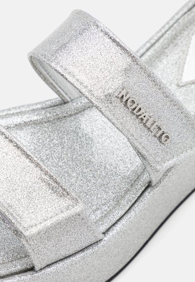 Silverglittrande sandaler med breda remmar och en framträdande logotyp. Slät yta med platt sula och minimalistisk design.