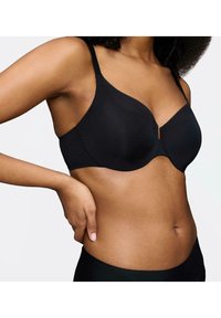 Soutien-gorge noir en tissu lisse et mat, avec armatures. Dispose de bretelles ajustables et d'un décolleté en V. Une paire de culottes noires unies est visible.