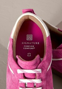 Roze napa tenisice s bijelim detaljima i vezanjem. Unutrašnjost ima svijetlu rozu podlogu s natpisom "SIGNATURE FOREVER COMFORT" u srebrnoj boji.