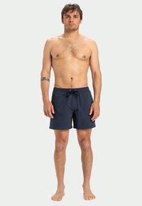 Tamsiai mėlynos maudymosi šortai su elastine juosta, su raišteliu ir šoninėmis kišenėmis. Lygus paviršius, aukščiau kelių ilgio.