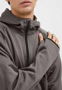 Felpa con zip grigia e colletto alto, realizzata in tessuto morbido. Presenta cuciture strutturate e dettagli neri sui polsini e sulla zip.