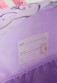 Lila tygväska med innerfack för namnlapp. Har rosa remmar och ett blommönster. Slät textur, med blixtlåsstängning.