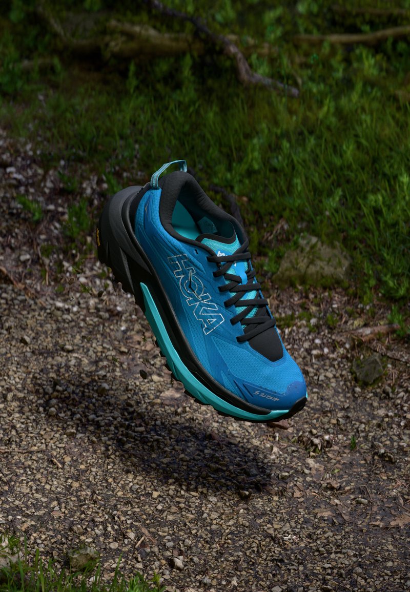 Zapatilla de correr azul y negra con parte superior de malla texturizada, cuello acolchado y suela Vibram, que presenta un acento turquesa y un intrincado patrón de tracción.