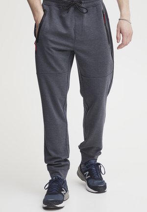 Pantalones atléticos grises con un acabado texturizado, bolsillos laterales y una cintura con cordón, combinados con zapatillas color marino.
