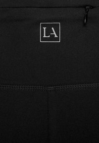 Schwarze Sporthosen mit einem silbernen "LA"-Logo. Glatter Stoff mit einer körperbetonten Passform und elastischem Bund, ausgestattet mit einer einzelnen Reißverschlusstasche.