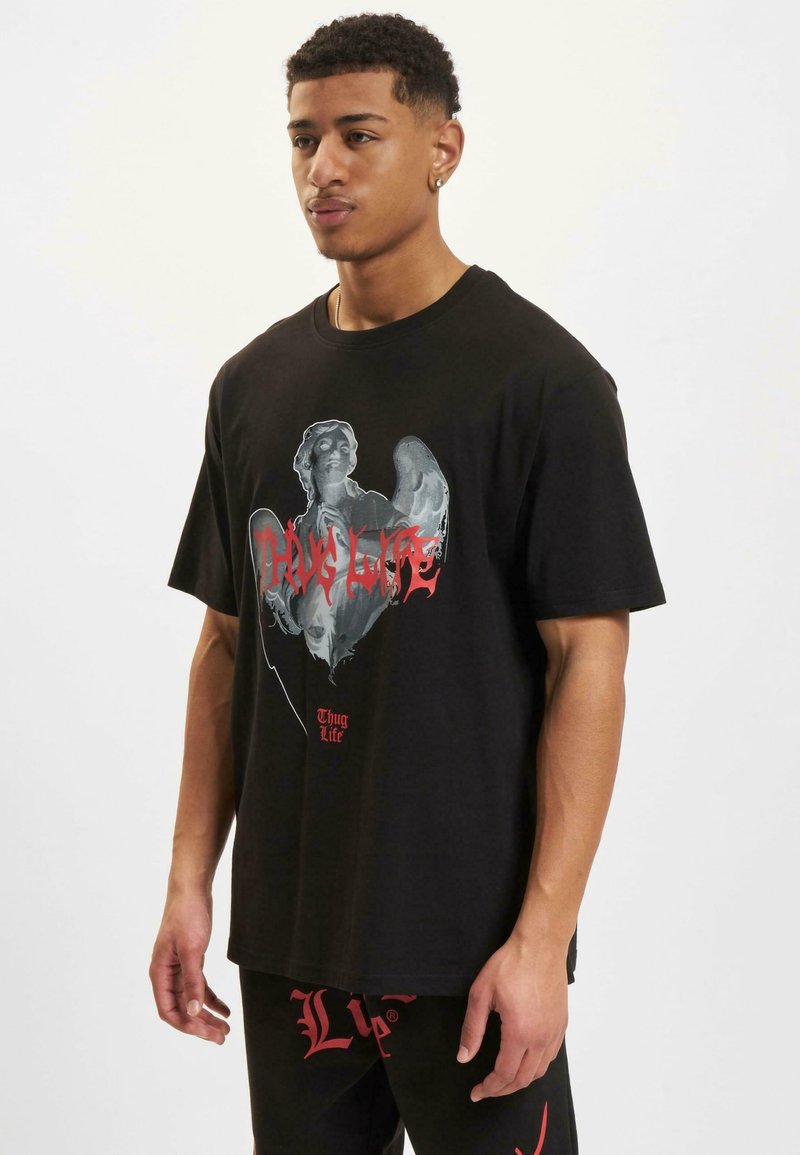 Čierne tričko s krátkym rukávom, ktoré má grafický potlač postavy s anjelskými krídlami a textom "Thug Life" v červenej farbe, umiestnené na svetlom pozadí.