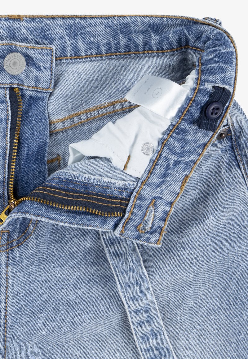 Jeans in denim blu chiaro con zip in ottone, chiusura a bottone, cuciture gialle a contrasto e un'etichetta in tessuto bianco visibile all'interno della vita.
