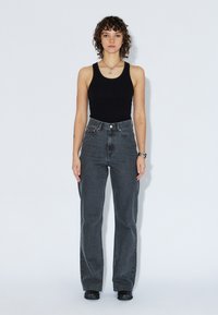 Top nero a canotta e jeans a vita alta con gamba dritta in denim grigio scuro. L'outfit presenta una chiusura a bottone e un design minimalista.