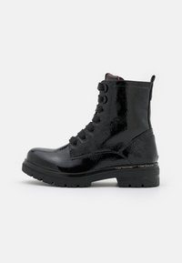 Bottines en cuir verni noir avec une finition haute et lisse, dotées de six œillets, de lacets noirs épais et d'une semelle robuste. Nom de la marque sur le talon.
