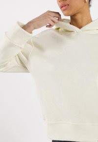 Felpa color crema con una texture morbida, vestibilità comoda e cappuccio ample e arrotondato. Presenta polsini e orlo a costine.