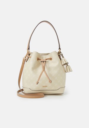 Beige Eimerhandtasche mit tanfarbenem Lederkordelzug, Schulterriemen und dekorativen Quasten vor einfarbigem Hintergrund.