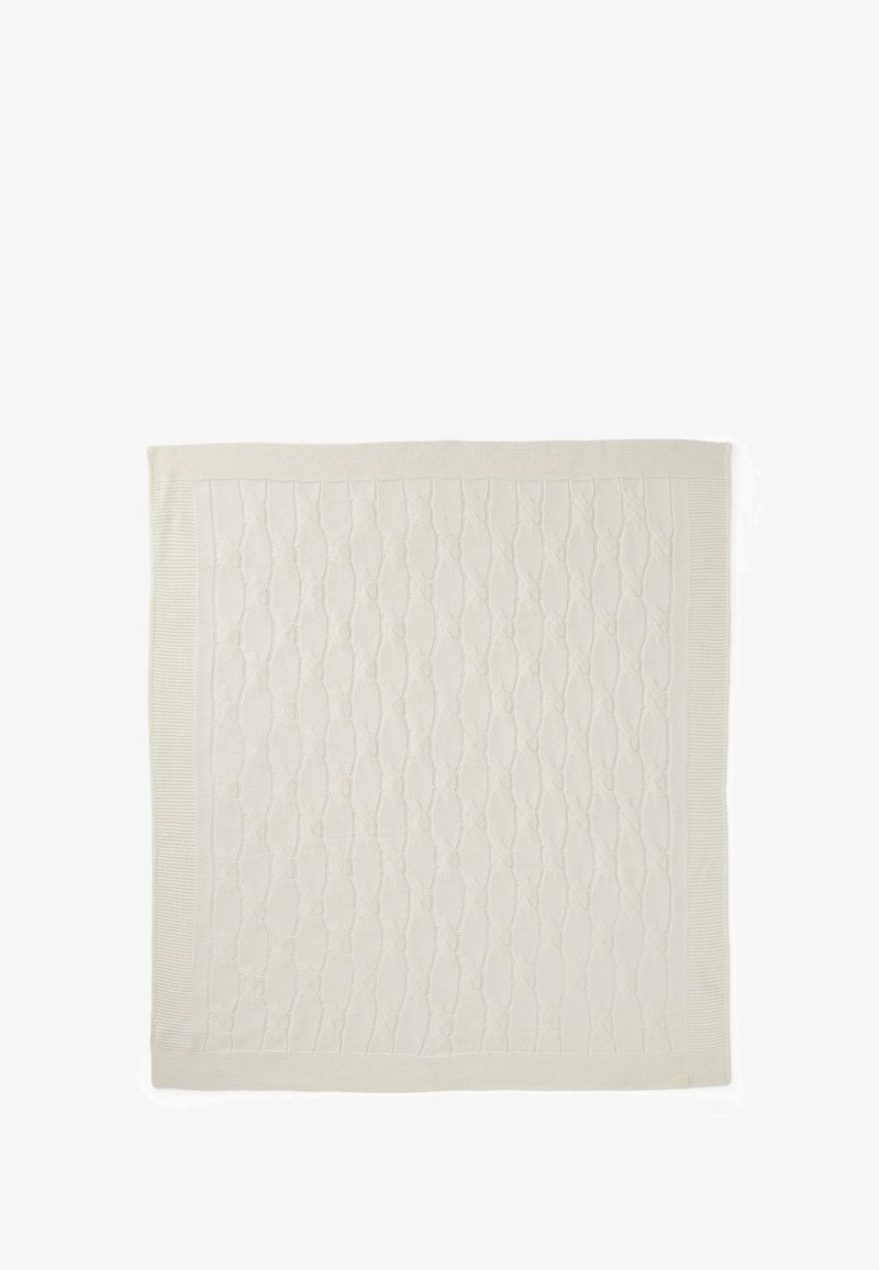 Krémová pletená deka s texturovaným kabelovým vzorem. Okraje jsou lemovány hladkým obložením, což ukazuje na jednotný tvar a barvu.