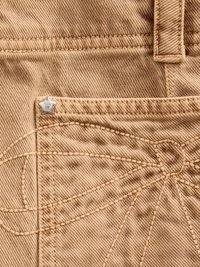 Beige denimstoff har en lomme med en stjernesformet sølvbeslag og dekorativ broderi i kontrastfarge.