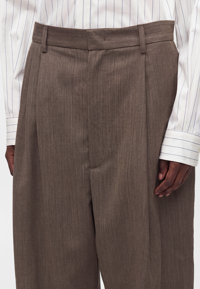 Pantalon large taille haute marron porté avec une chemise blanche à manches longues avec fines rayures verticales et poignets boutonnés.