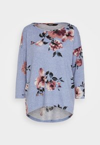 Långärmad, blå blus med stora rosa och vinröda blommor, rundad halsringning och en asymmetrisk nederkant. Tillverkad av mjukt, texturerat tyg.