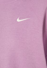 Närbild av ett ljuslila tyg med en liten vit Nike swoosh-logga broderad nära den övre mitten.
