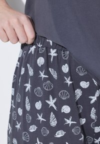 Grau Baumwollkleid mit gerafftem Bund, das ein bedrucktes Muster aus Muscheln und Seesternen in Weiß zeigt. Nahaufnahme, die das Taschen-Detail zeigt.