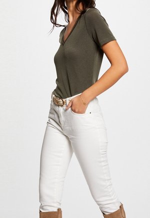 Haut olive vert à manches courtes et col en V associé à un pantalon blanc ajusté et une ceinture à motifs. La tenue présente une texture lisse et un design décontracté.