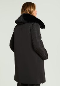 Abrigo acolchado negro de silueta larga, con un gran cuello de piel sintética, textura suave y mangas acolchadas. Bolsillos frontales con cremallera.