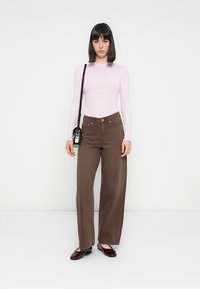 Bruine wijde broek met knoopsluiting, gecombineerd met een aansluitend lichtroze geribbeld langemouwen T-shirt en een zwarte schoudertas. Bordeaurode flats.