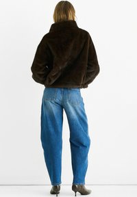 Brown faux fur jacket with a high collar, paired with loose-fit blue jeans showing a gradual lightening effect and rounded back pockets.