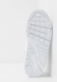 Suela de zapatilla Nike blanca que presenta un diseño de goma texturizada con tacos prominentes y un borde curvado suave. "ANTIMARCA" grabado en el lateral.