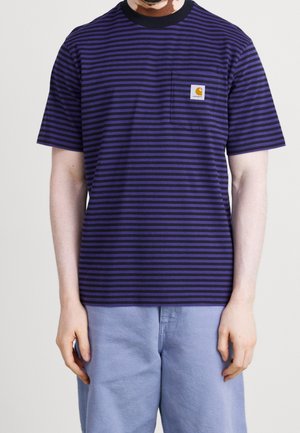 Man draagt een paars-zwart horizontaal gestreept T-shirt met korte mouwen, een klein borstzakje en lichtblauwe broek.