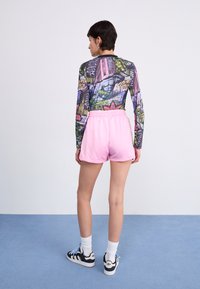 T-shirt graphique à manches longues présentant des couleurs vives et des motifs urbains, associé à un short en coton rose. Le modèle porte des baskets noires avec des lacets bleus.