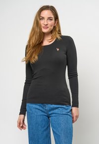 Svart långärmad ribbad topp med rundad halsringning; har en liten broderad detalj. Kombinerad med ljusblå vida jeans.