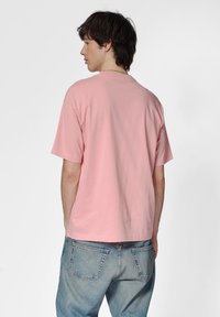 Ljust rosa bomull t-shirt med korta ärmar, rund halsringning och en avslappnad passform, parat med blå denimjeans med bakfickor.