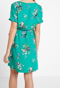 Grünes Blumenkleid mit kurzen Ärmeln, Rüschensaum, taillierter Taille und lockerem Schnitt. Es zeigt verschiedene bunte Blumen- und Schmetterlingsmuster.