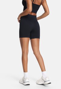 Crni sportski set s majicom i kratkim hlačama, izrađen od glatkog, rastezljivog materijala. Kratke hlače imaju visok struk i uski kroj. Bijele tenisice i čarape.