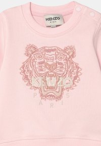 Sudadera rosa con cuello redondo, que presenta un diseño de tigre bordado y el texto "KENZO PARIS" debajo. Tejido suave, puños acanalados.