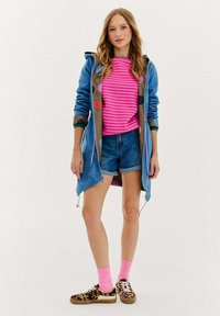 Niebieska kurtka z kapturem i wzorzystą podszewką, różowa bluzka w paski, dżinsowe szorty, różowe skarpetki i buty w wzór pantery. Luźna, warstwowa stylizacja.
