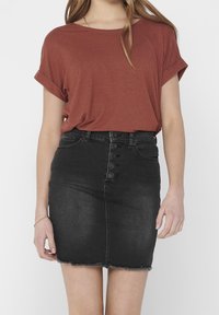 Rustrød T-shirt med oprullede ærmer, parret med en sort denimnederdel med knaplukning foran og frynset kant.