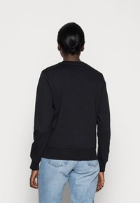 Černá mikina s kulatým výstřihem a žebrovanými manžetami, kombinovaná se světle modrými džíny. Hladká textura, volný střih, minimalistický design.