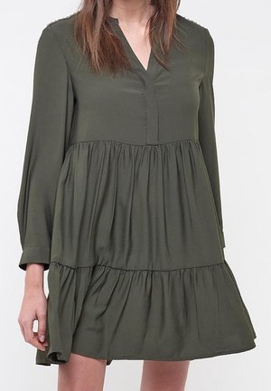 Vestido verde oliva de manga larga, con escote en V y dobladillo con volantes en capas. Fabricado con un material suave y fluido, de corte holgado.
